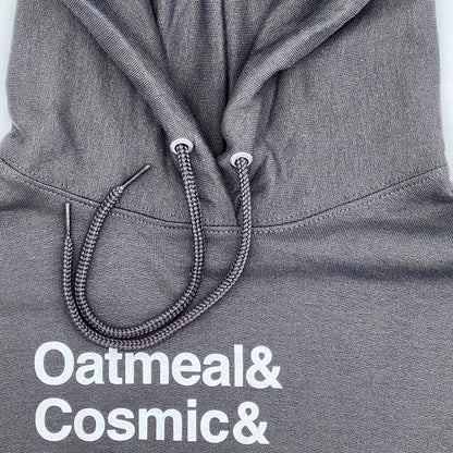 Close-up view of the top part of a Little Debbie Fan Favorites gray hoodie. The fabric displays a finely knit texture, and the drawstrings are braided with metal aglets. Just below the drawstrings, white text reads 'Oatmeal& Cosmic&'.